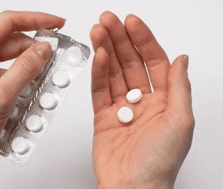 يد شخص تقوم بأخذ حبتين دواء من ظرف يحتوي على عدة حبوب بيضاء اللون في داخله