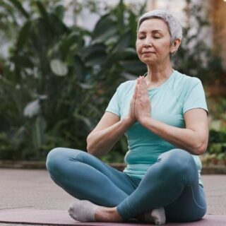 امرأة ذات شعر أبيض تقوم بالاسترخاء وهي تمارس اليوجا في حديقة منزلها