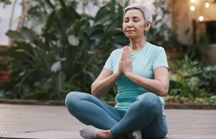 امرأة ذات شعر أبيض تقوم بالاسترخاء وهي تمارس اليوجا في حديقة منزلها