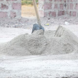 كومة من الإسمنت البورتلاندي الجاف موجودة على الأرض في غرفة يتم بنائها وعلى كومة الإسمنت الجاف يوجد رفش