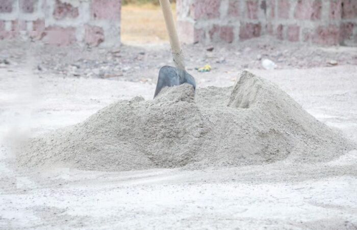 كومة من الإسمنت البورتلاندي الجاف موجودة على الأرض في غرفة يتم بنائها وعلى كومة الإسمنت الجاف يوجد رفش