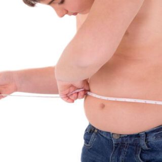 طفل سمين يظهر نصف عارياً يلبس بنطلون جينز أزرق اللون ويلف شريط قياس حول بطنه وهو ينظر للرقم الظاهر على شريط القياس