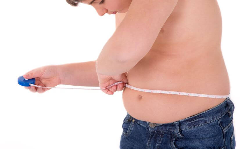 طفل سمين يظهر نصف عارياً يلبس بنطلون جينز أزرق اللون ويلف شريط قياس حول بطنه وهو ينظر للرقم الظاهر على شريط القياس