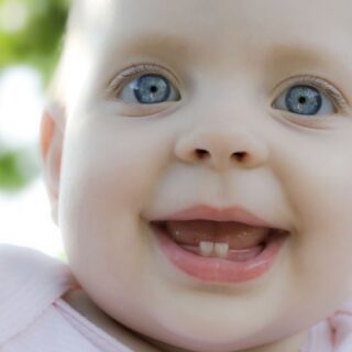 طفل صغير عيونه زرقاء يضحك و قد بدأت اثنان من اسنانه السفلية بالظهور