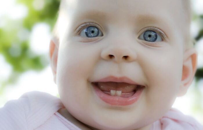 طفل صغير عيونه زرقاء يضحك و قد بدأت اثنان من اسنانه السفلية بالظهور