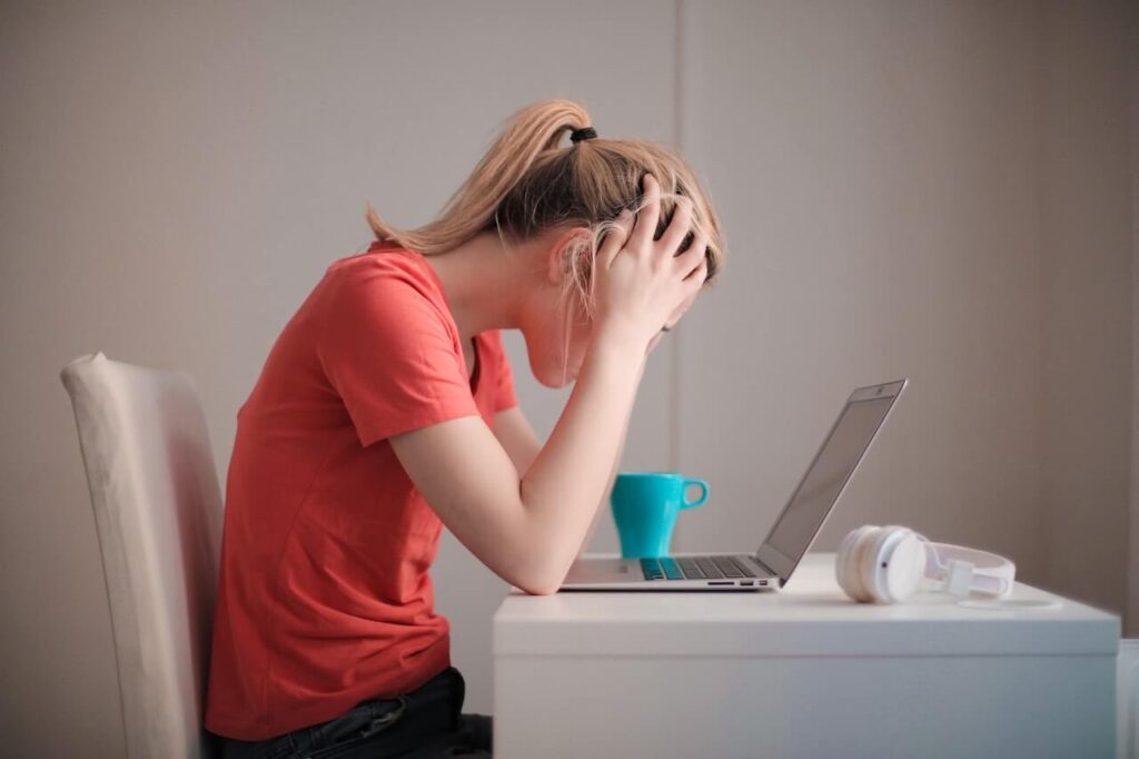 امرأة متوترة تجلس على الطاولة امام شاشة الحاسب وتضع يديها على رأسها