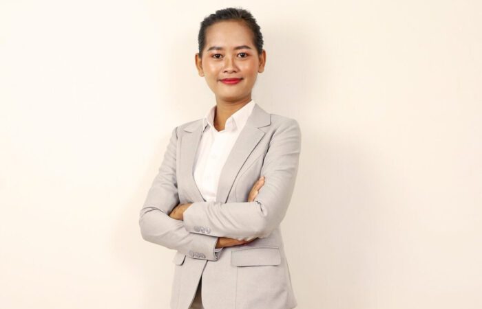 امرأة أسيوية في ثياب العمل الرسمية ذات اللون الرمادي الفاتح تقف واثقة من نفسها