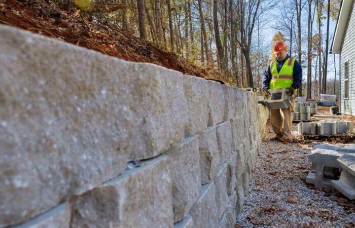 عامل بناء يقوم ببناء جدار استنادي حول المنزل لمنع انهيار التربة واقترابها من المنزل