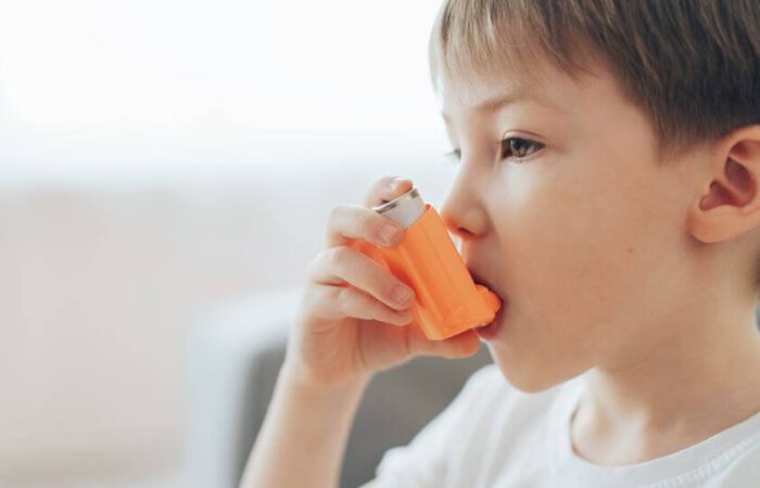 طفل يلبس كنزة بيضاء ويضع على فمه جهاز بخاخ لونه أورانج يحتوي على دواء للربو القصبي