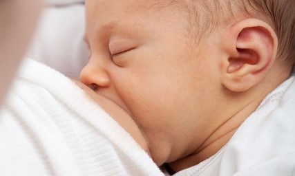 طفل رضيع يلبس كنزة بيضاء اللون ويقوم برضاعة الحليب من صدر أمه وهي تنظر اليه
