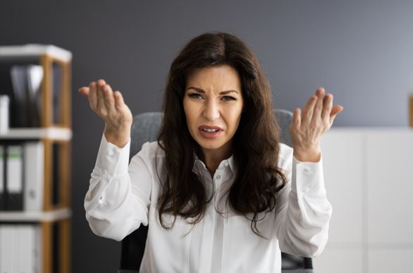 امرأة جالسة في المكتب و تلبس قميص عمل أبيض اللون وتقوم بالإشارة بتعجرف اتجاه الشخص الجالس امامها