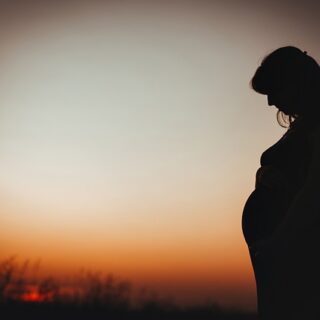 امرأة حامل تقف في الخارج بعد غياب الشمس وهي تنظر الى بطنها بتأمل