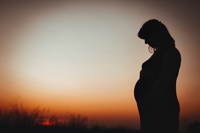 امرأة حامل تقف في الخارج بعد غياب الشمس وهي تنظر الى بطنها بتأمل