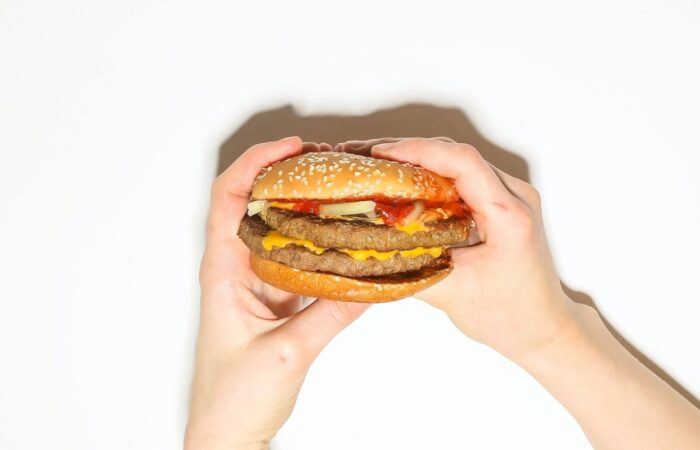يدان تمسكان بقطعة هامبرغر محشوة باللحمة والبطاطا