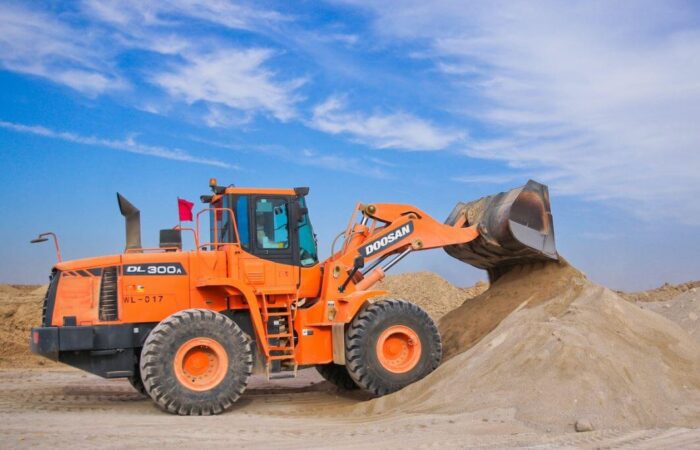 بلدوزر كبير له دواليب ولونه أورانج يقوم بتجميع الرمل على شكل تلة في يوم مشمس