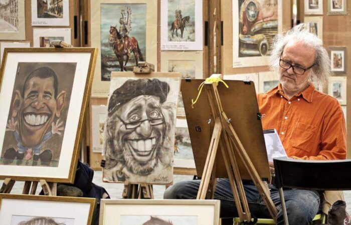 رسام كاريكاتير يضع نظارات وشعره أبيض يقوم برسم لوحات كاريكاتيرية وهو جالس في ورشته