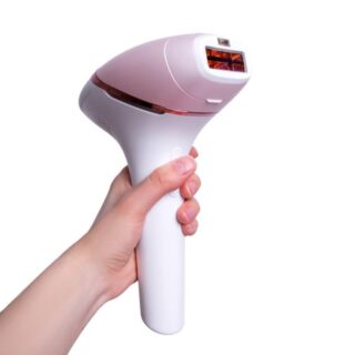 يد فتاة تُمسك بجهاز ليزر منزلي لإزالة الشعر ويظهر هذا الجهاز باللون الزهري والأبيض