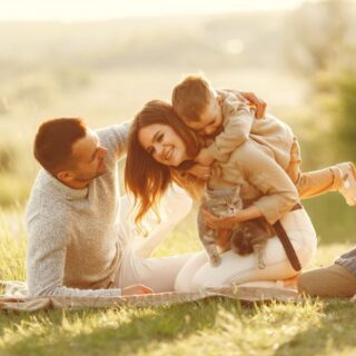 عائلة مؤلفة من أربعة أشخاص هم الأب والأم و ولدين يجلسون على العشب في حديقة ويظهر الولد الصغير فرحاً وهو يمتطي ظهر والدته