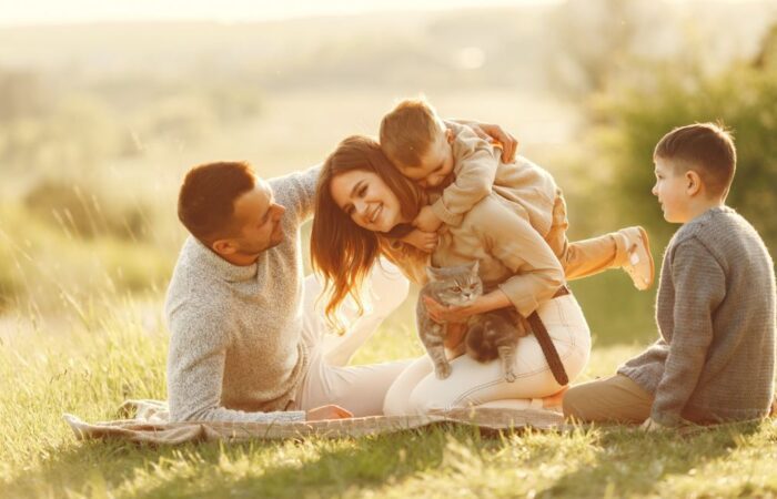 عائلة مؤلفة من أربعة أشخاص هم الأب والأم و ولدين يجلسون على العشب في حديقة ويظهر الولد الصغير فرحاً وهو يمتطي ظهر والدته