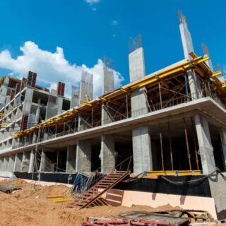 بناية يتم بنائها وتظهر الأعمدة والأسقف الإسمنتية دون جدران ويوجد أمام البناية مواد بناء بالإضافة لرافعة صفراء كبيرة