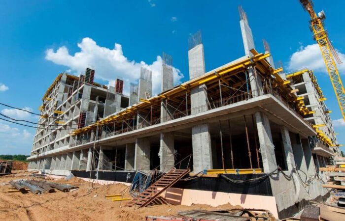 بناية يتم بنائها وتظهر الأعمدة والأسقف الإسمنتية دون جدران ويوجد أمام البناية مواد بناء بالإضافة لرافعة صفراء كبيرة