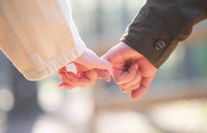 شاب وفتاة يشبكون الأصبع الصغير ليديهم ويسيرون مع بعضهم البعض