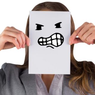 امرأة بالغة تمسك بورقة مرسوم عليها ايموجي لوجه سيئ وتضع المرأة هذه الورقة أمام وجهها