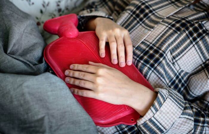 فتاة تضع كيس مياه دافئ أحمر اللون على بطنها وهي متمددة بسبب معاناتها من عسرة الطمث