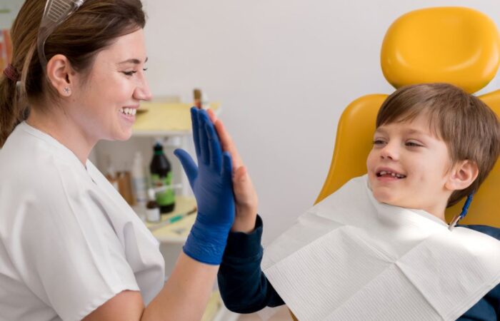 طبيبة أسنان تلبس قفاز مطاطي أزرق اللون وتضع كف يدها على كف يد طفل جالس أمامها من ذوي الاحتياجات الخاصة