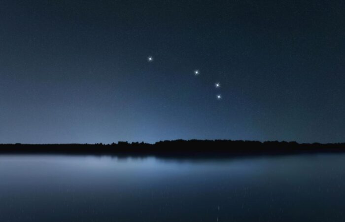 ليلة صافية في الخارج بالقرب من بحيرة وتظهر في السماء المظلمة أربعة بقع ساطعة باللون الأبيض