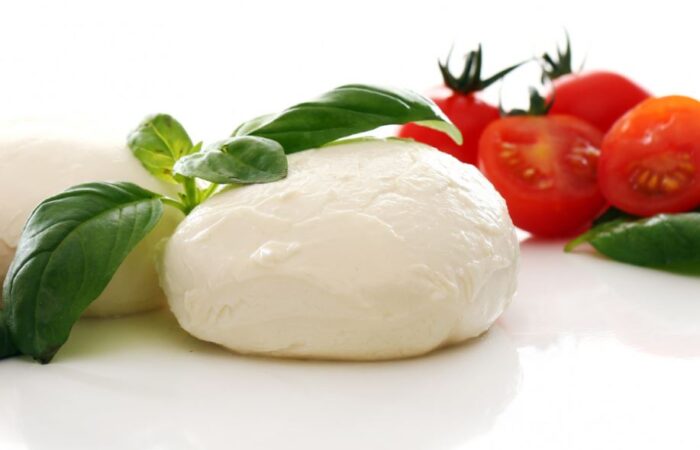 قرص جبنة كروي وأبيض اللون وبجانبه قطع من البندورة الحمراء و أوراق الريحان الخضراء