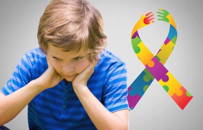 صبي صغير يلبس كنزة زرقاء ويجلس وحيداً ويضع يديه على خده وهو ينظر للأسفل وبجانبه شعار مرض التوحد الملون باللون الأزرق والأصفر والأحمر الفاتح