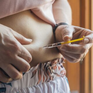 امرأة بالغة تقوم بالكشف عن بطنها وحقن نفسها بمادة الأنسولين عن طريق حقنة طبية صفراء اللون