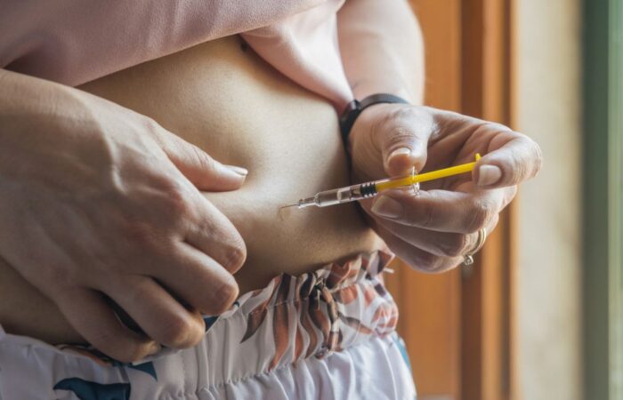 امرأة بالغة تقوم بالكشف عن بطنها وحقن نفسها بمادة الأنسولين عن طريق حقنة طبية صفراء اللون