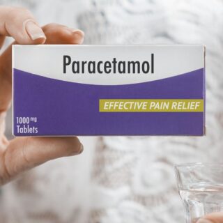 علبة دواء الباراسيتامول لونها بنفسجي وأبيض مكتوب عليها اسم الدواء باللغة الإنكليزية و تمسك بهذه العلبة امرأة