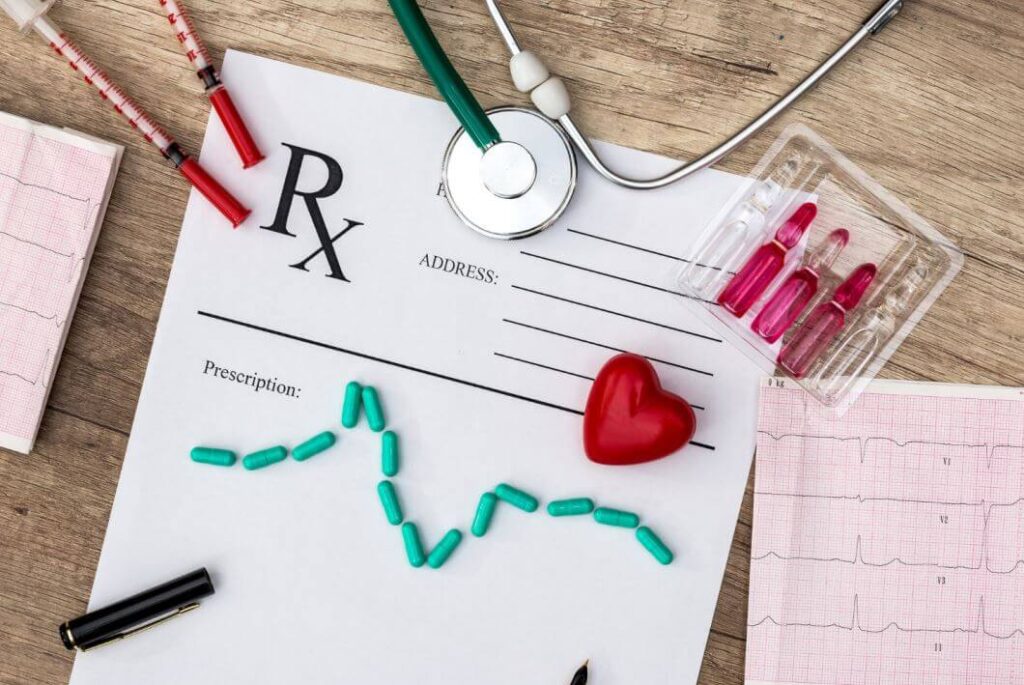سماعات الطبيب وعينات من الدم و ورقة تخطيط للقلب بالإضافة لقلب أحمر و ورقة بيضاء موضوعين على طاولة لونها بني فاتح