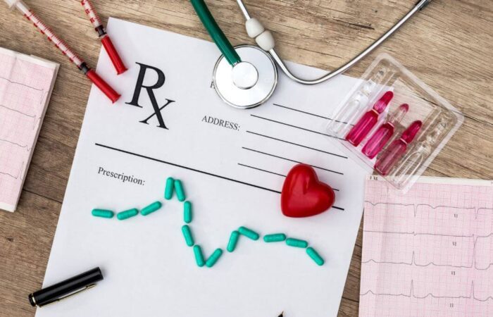 سماعات الطبيب وعينات من الدم و ورقة تخطيط للقلب بالإضافة لقلب أحمر و ورقة بيضاء موضوعين على طاولة لونها بني فاتح