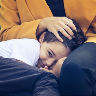 صبي صغير يجلس في حضن والدته ويبتسم بخجل وتقوم الأم بوضع يدها على رأسه