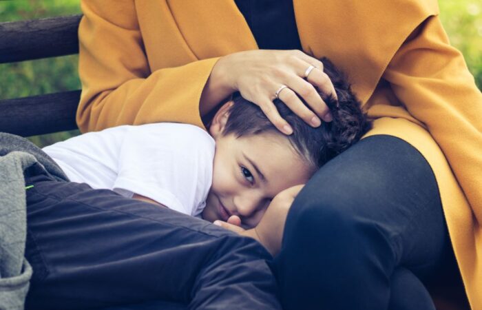 صبي صغير يجلس في حضن والدته ويبتسم بخجل وتقوم الأم بوضع يدها على رأسه