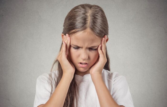 فتاة صغيرة تلبس كنزة بيضاء وتضغط بأصابع يديها على جانب رأسها بسبب احساسها بالألم في رأسها