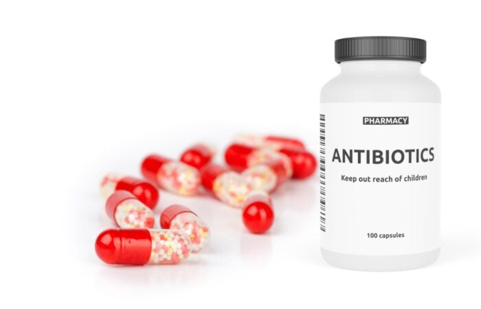 علبة دواء للمضادات الحيوية اسطوانية الشكل وبجانبها حبوب دواء ملونة باللون الأحمر و الأبيض الشفاف