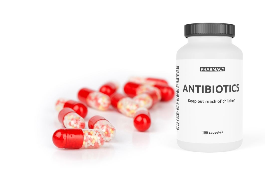علبة دواء للمضادات الحيوية اسطوانية الشكل وبجانبها حبوب دواء ملونة باللون الأحمر و الأبيض الشفاف