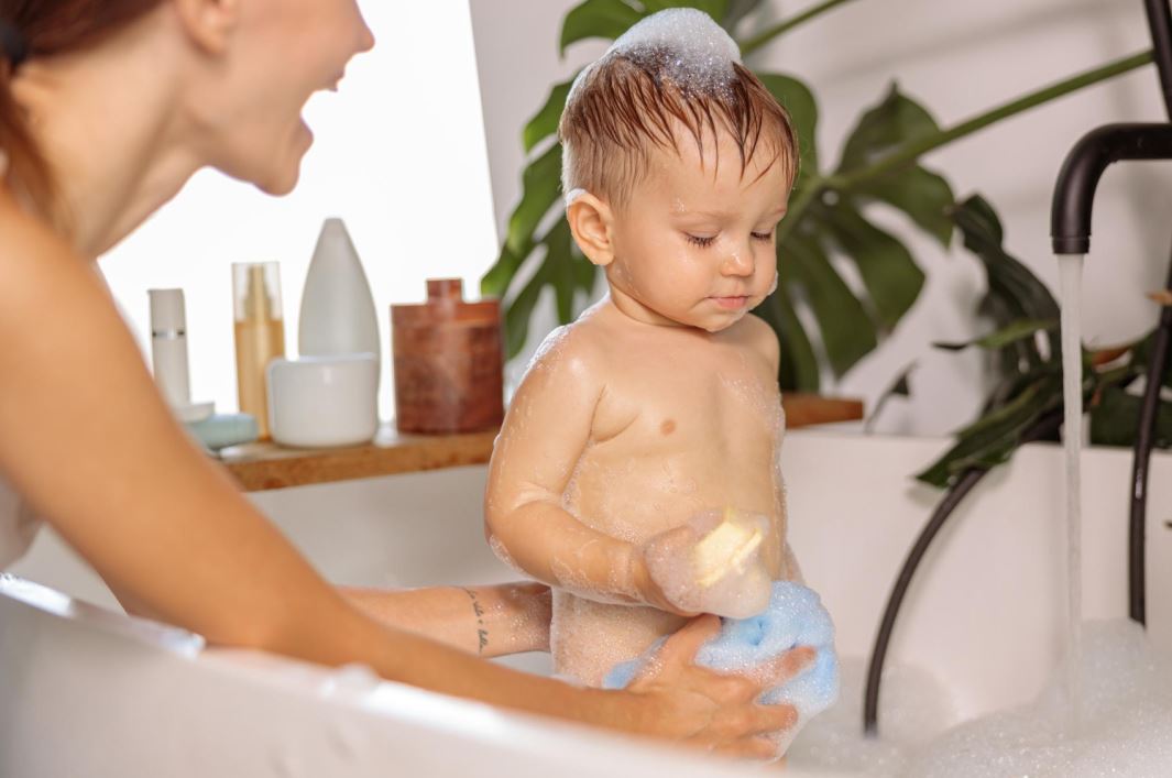 طفل صغير يقف في مغطس الاستحمام وتقوم الأم بمساعده في الاستحمام