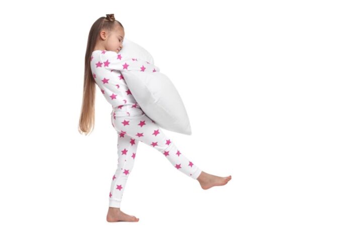 فتاة صغيرة ترتدي ملابس النوم وتقوم بالمشي وهي نائمة وتقوم بحضن مخدة بيضاء اثناء مشيها
