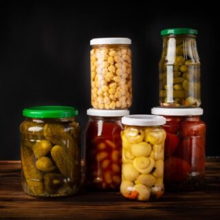 مجموعة من العلب الزجاجية شفافة اللون بداخلها خضار متنوعة كالخيار والفطر والفول والحمص