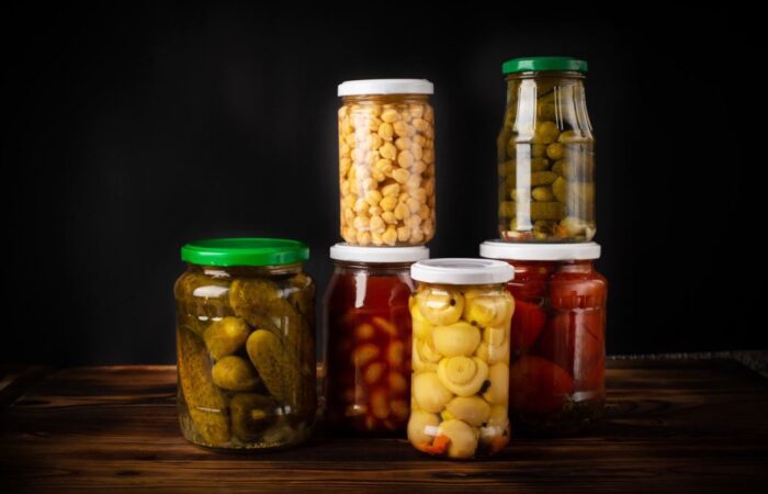 مجموعة من العلب الزجاجية شفافة اللون بداخلها خضار متنوعة كالخيار والفطر والفول والحمص