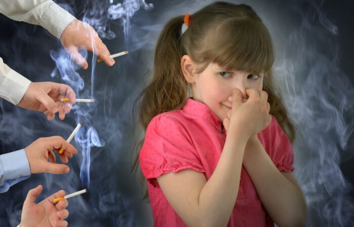 فتاة صغيرة ترتدي قميص أحمر تقوم بسد أنفها بسبب تدخين العديد من الأشخاص من حولها للسجائر