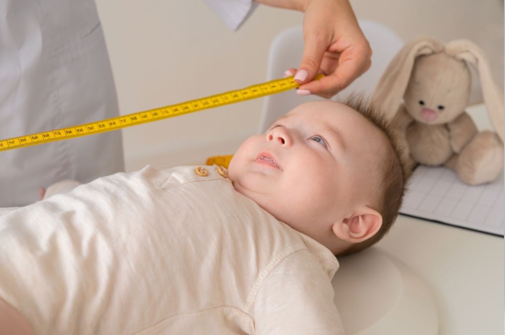 طفل رضيع يستلقي على ظهره في عيادة الأطفال ويقوم الطبيب بقياس طوله