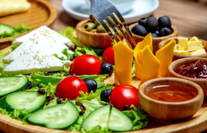 صحن خشبي يحتوي على جبنة الشيدر الصفراء على شكل شرحات ملفوفة بشكل اسطواني وبجانبها قطع من الخيار والبندورة والزيتون الأسود، ويقوم شخص بتناول قطع جبنة الشيدر بالشوكة