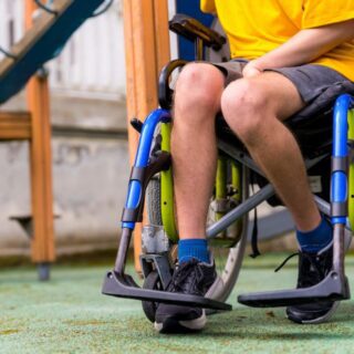 صبي مصاب بالشلل يجلس على كرسي متحركة لها دواليب وهو موجود في ساحة للعب الأطفال